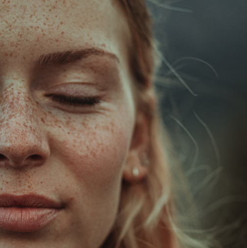Close-up of a young woman with freckles, closed eyes, and pink lips, side of face visible.