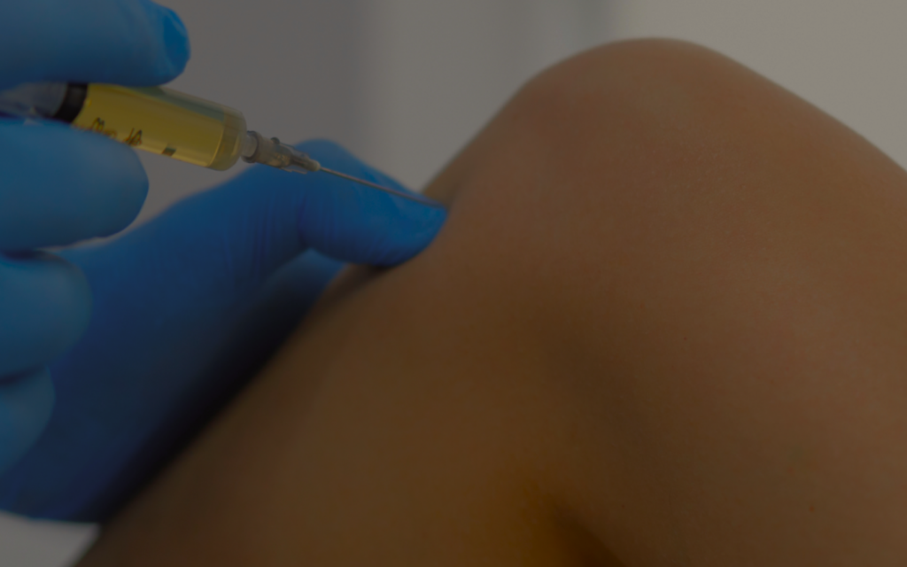 Close-up of a gloved hand with a syringe injecting into a person's upper arm.