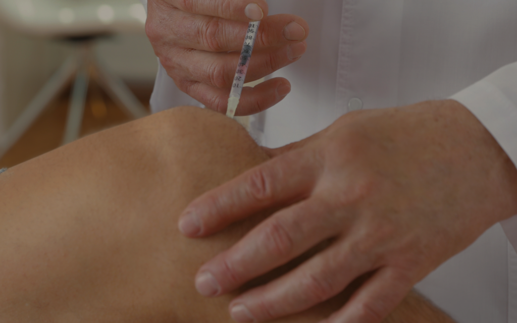 Medical professional administering an injection into a patient’s buttock with a syringe.