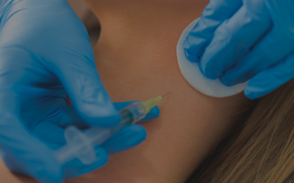 Medical professional in blue gloves injects syringe into the back of a patient’s neck.