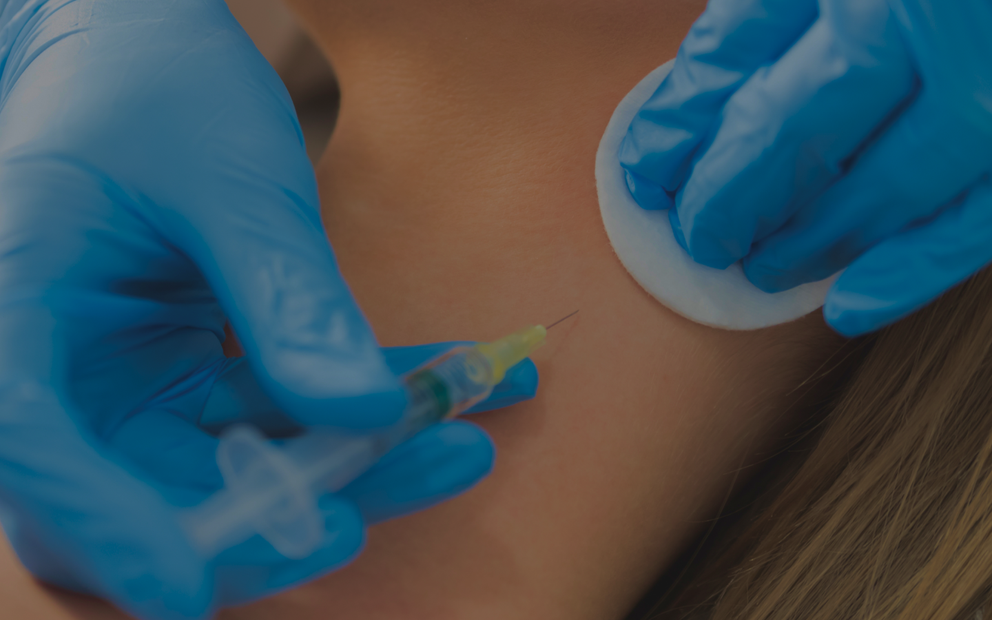Medical professional in blue gloves injects syringe into the back of a patient’s neck.