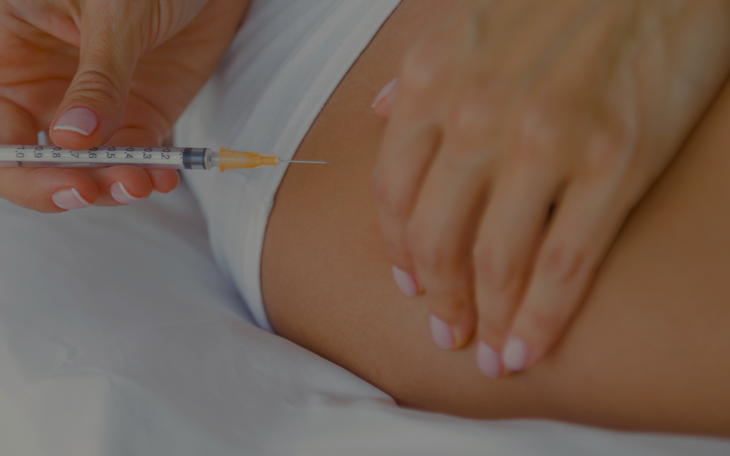 Close-up of a syringe nearing a person's exposed skin while a caregiver stabilizes the area for injection.