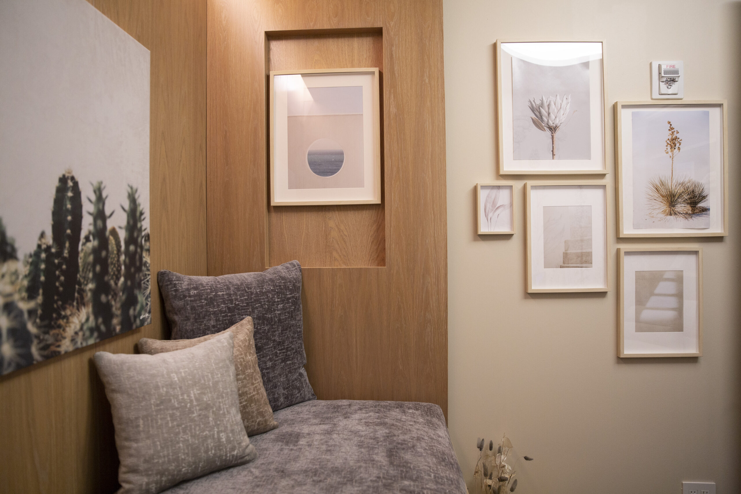 Cozy nook with gray upholstered bench and two textured cushions against wood-paneled wall, framed art on wall.