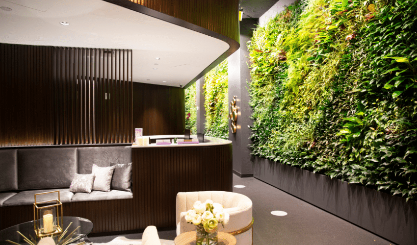 Lobby with curved wood reception, gray seating, and a vertical green plant wall.
