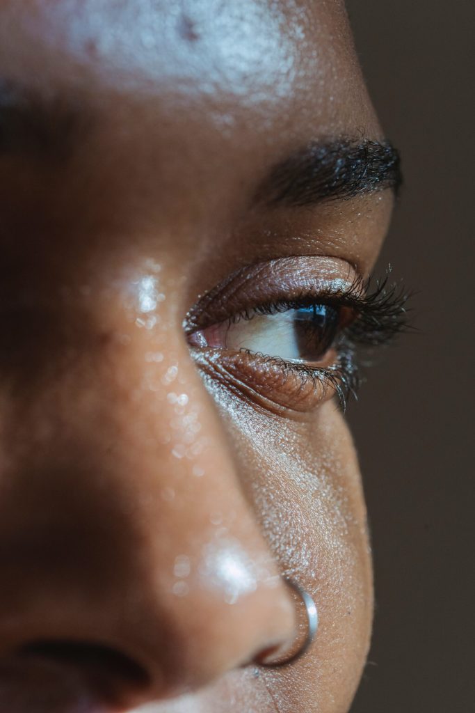 Close-up of a dark-skinned person's eye in profile, with long lashes and a nose ring.