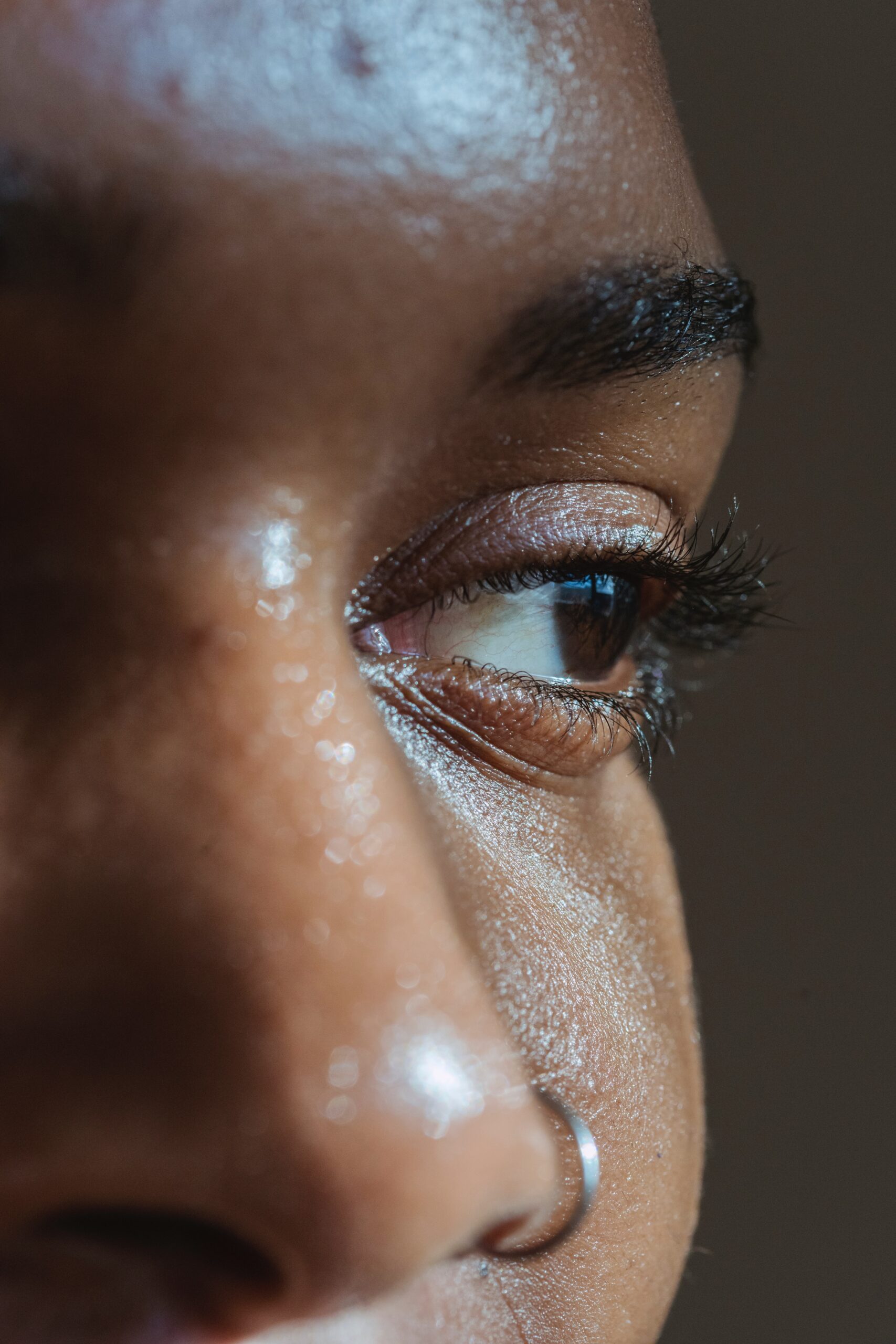 Close-up of a dark-skinned person's eye in profile, with long lashes and a nose ring.