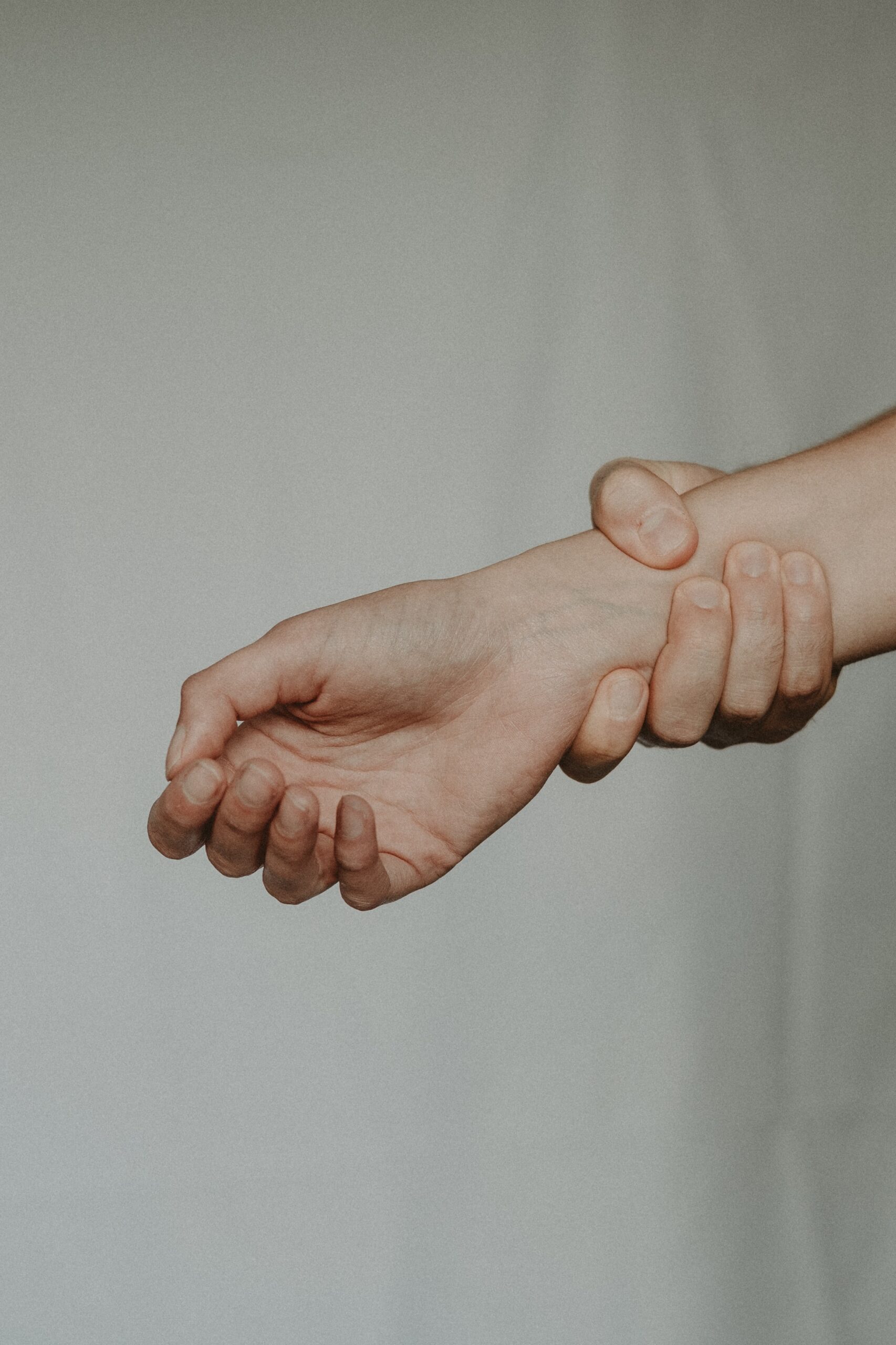 Two hands holding each other, one gripping the other's wrist against a plain background.