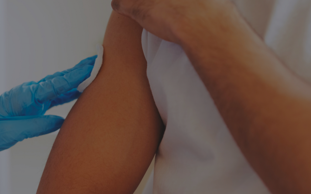 Medical professional in blue gloves swabbing a person's upper arm with gauze or pad.