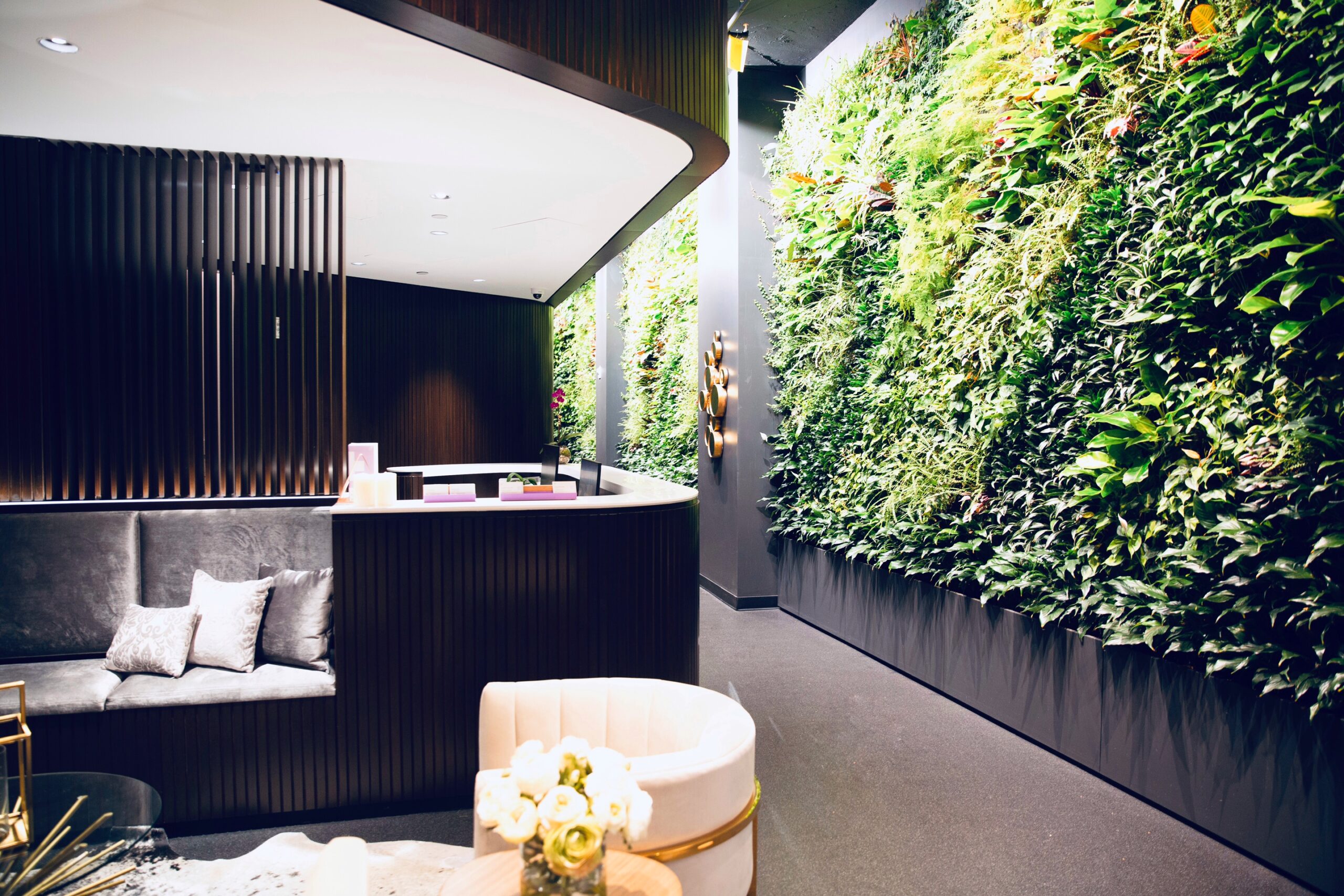 Modern lobby with dark vertical panels, curved reception desk, and a tall living green wall.