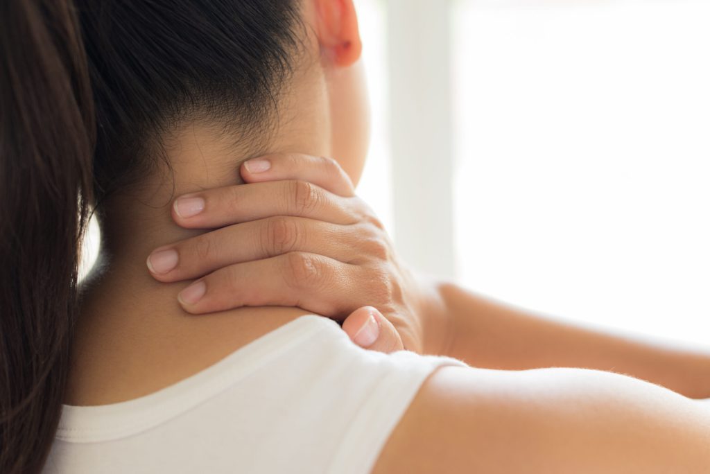 Back of a person's neck being supported by hands, white sleeveless top, bright background.