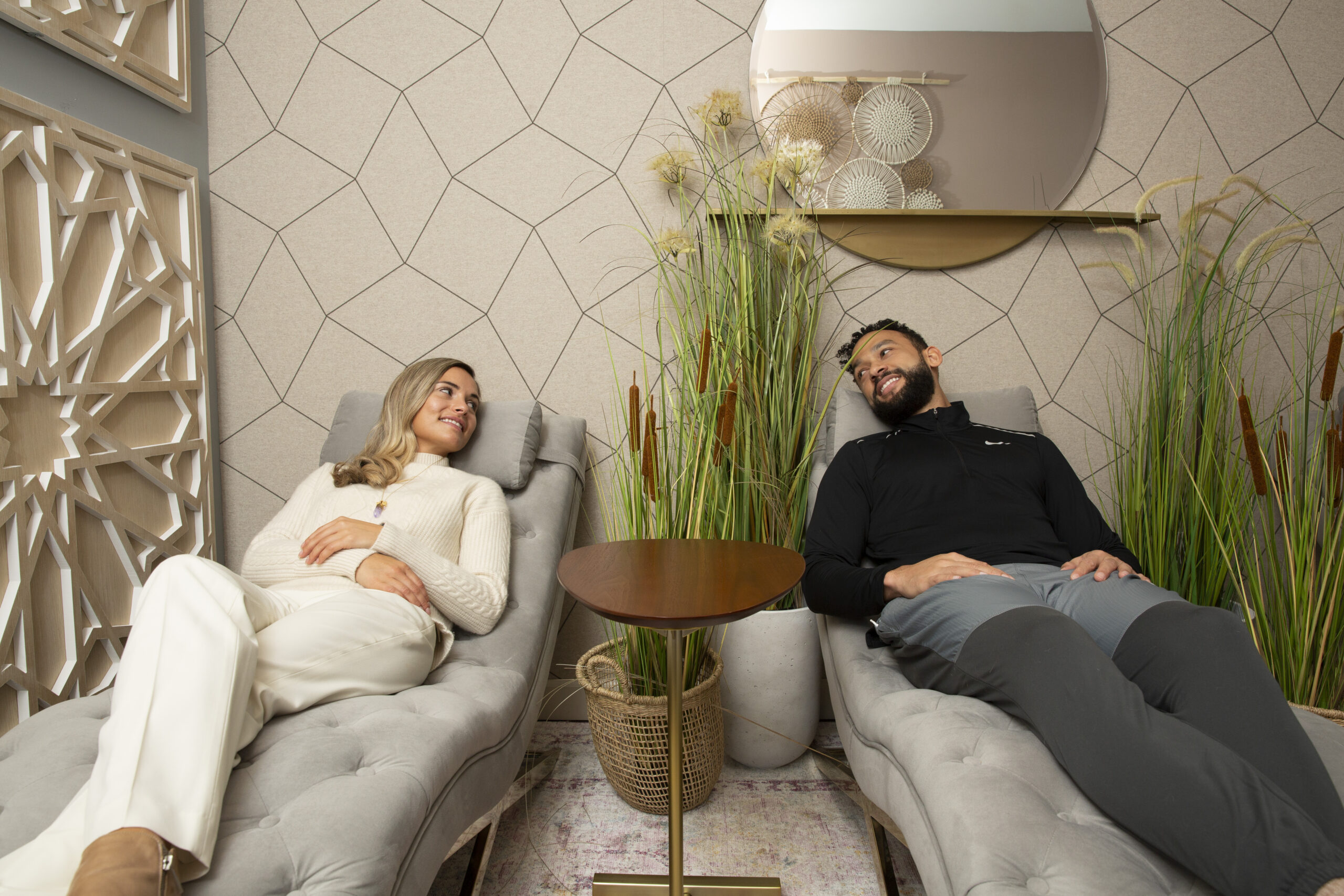 Two people reclining on gray lounge chairs in a stylish room with a small round table between them.