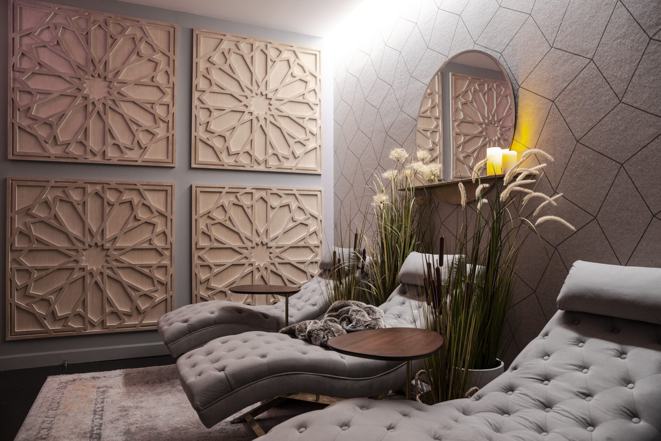 Relaxation lounge with tufted gray chaise, geometric wall panels, round mirrors, and candles.