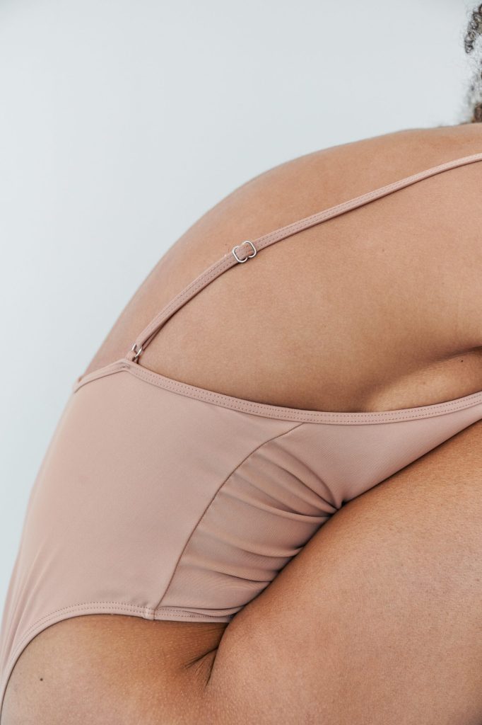 Close-up of a light pink bra strap on a curvy back, with smooth fabric and stitching.