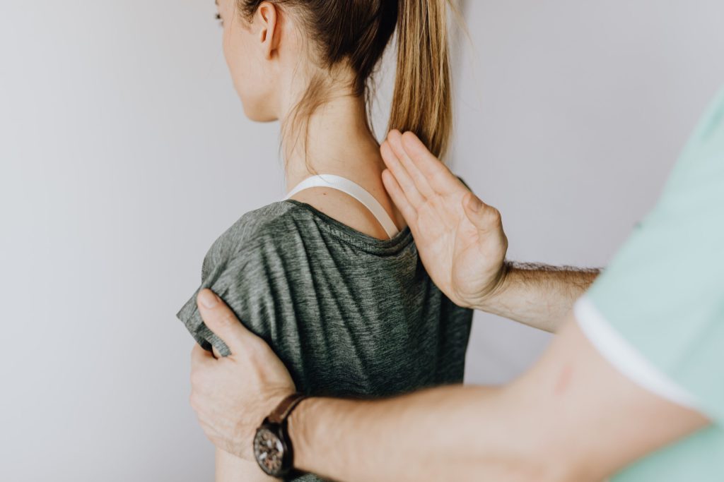 Person in a gray shirt is supported from behind by another hand on upper back and shoulder.