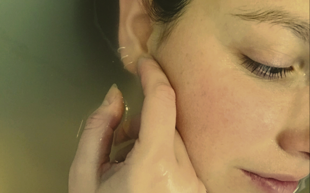Close-up of a woman's face with closed eye, hand touching her ear/neck area.