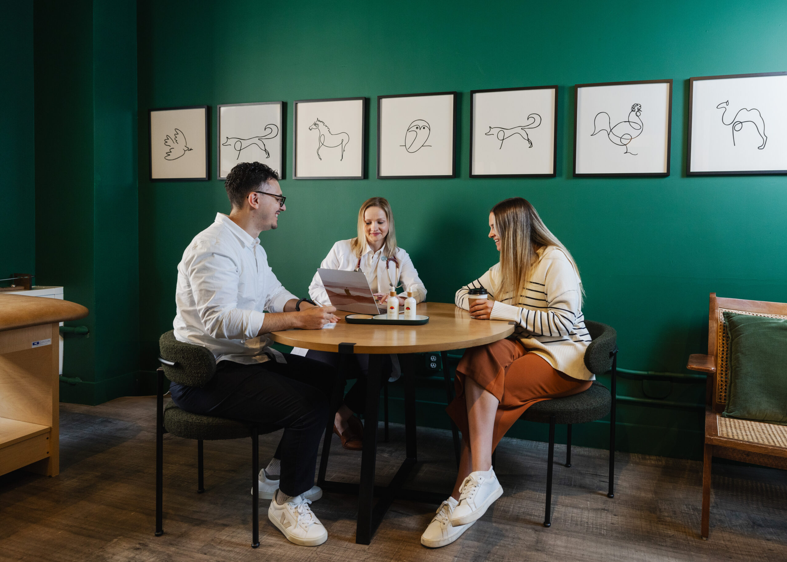 Three people at a round table in a green room review documents and a tablet.