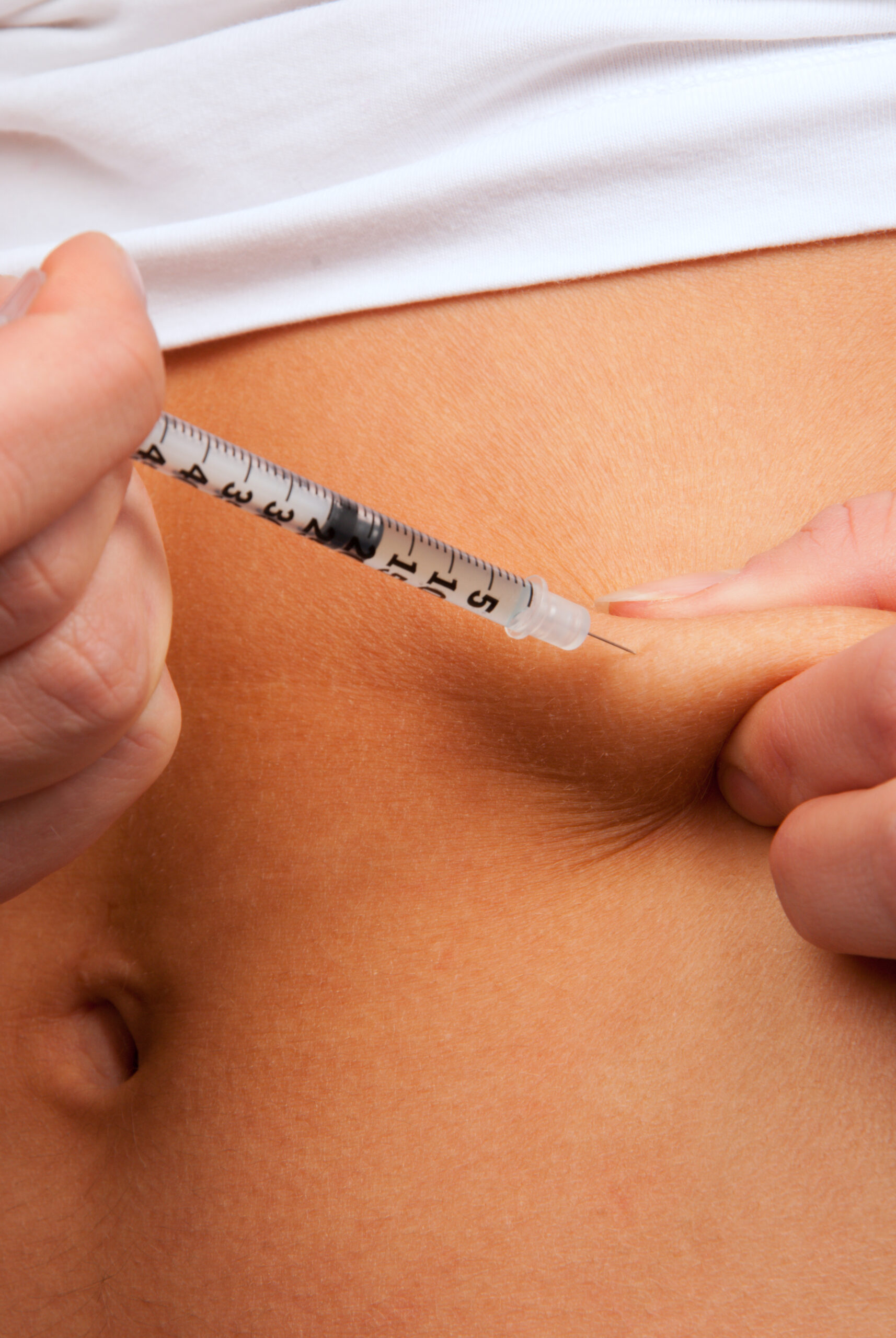 Close-up of a syringe being inserted into the skin on a person's abdomen.