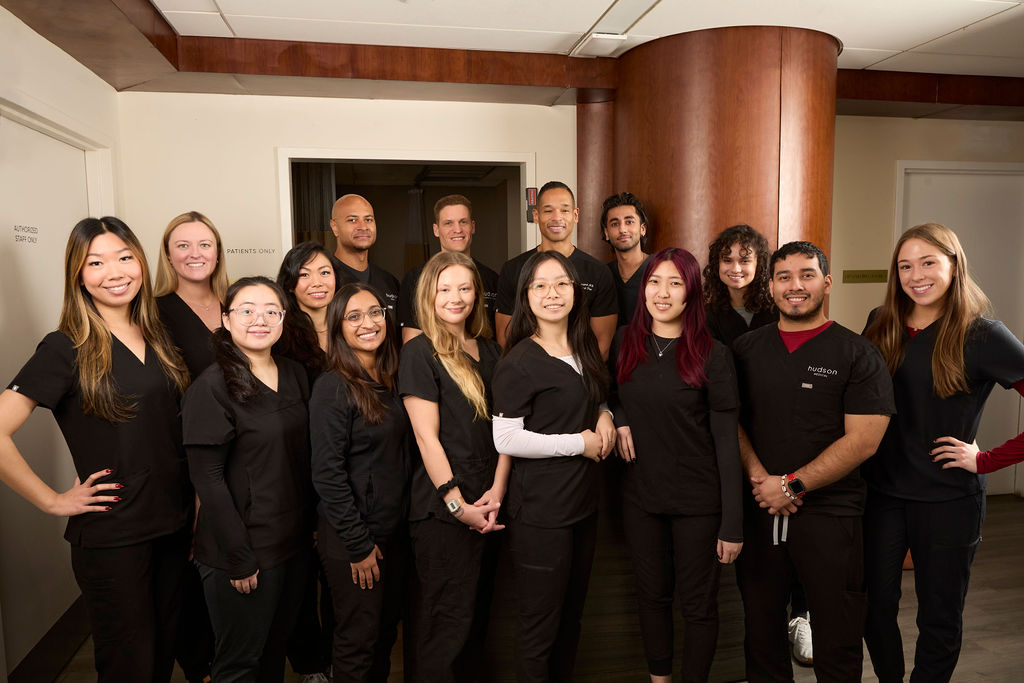 Group of diverse healthcare students in black scrubs posing indoors in a hallway.